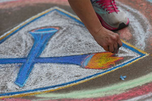 a closeup of an artist's hand drawing the Emory shield in chalk on a sidewalk