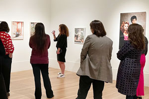 in an art gallery, people are facing away from the camera to view art on the walls